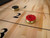 Doc & Holliday Paula Parsons Shuffleboard Table, Glazed Maple, available in 9 ft and 12 ft sizes, with red and metallic pucks positioned on the natural wood surface.