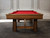Doc & Holliday Hank Slate Pool Table – Americana Chocolate, a wooden pool table with a red felt surface and black corner accents, in a stylish room with decorative wall paneling.