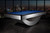 Doc & Holliday Poshy Pool Table | Reverse Rainbow Edition, modern pool table with a sleek grey and black design featuring a bright blue playing surface, set against a city skyline at sunset.
