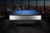 Doc & Holliday Poshy Pool Table | Reverse Rainbow Edition, modern pool table with a blue playing surface and sleek silver and black design in a high-rise setting with city skyline view at dusk.