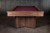 Doc & Holliday Arthur Deco Walnut Pool Table, classic wooden pool table with a walnut finish and red felt surface, set against a dark textured wall.
