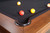 Doc & Holliday Muse Pool Table, made in USA, featuring a close-up of the corner with a black bumper and multi-colored billiard balls on the black felt surface.