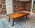 Doc & Holliday Muse Pool Table, made in USA, with an orange felt surface and wooden frame, set up in a stylish room with patterned wallpaper and a colorful geometric carpet.