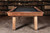 Doc & Holliday Muse Pool Table, made in USA, wooden pool table with black felt surface against a background of bookshelves filled with books.