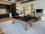 Doc & Holliday George Slate Pool Table by Doc & Holliday, showcasing a modern pool table with a grey walnut finish placed in a contemporary living room with stylish furniture and decor.