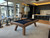 Doc & Holliday George Slate Pool Table by Doc & Holliday in Grey Walnut, situated in a modern game room with large windows, bar stools, and a kitchen island.