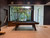Doc & Holliday George Slate Pool Table by Doc & Holliday, featuring a sleek grey walnut finish in a modern interior space with large windows and greenery outside.