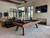 Doc & Holliday George Slate Pool Table by Doc & Holliday, featuring a grey walnut finish, in a modern game room with a TV, couch, and large windows.