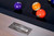 Doc & Holliday George Slate Pool Table by Doc & Holliday with Glazed Pearl finish, close-up of the brand's metallic logo plate and billiard balls on the table's surface.