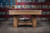 Doc & Holliday Hank Slate Pool Table, rustic silver brown oak with a sturdy wooden frame and slate surface, in front of a patriotic metal wall background.