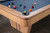 Doc & Holliday Preakness Pool Table in Maple, close-up of corner showing the wooden frame, black ball return, and billiard balls on the felt playing surface.