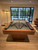 Doc & Holliday Preakness Pool Table in Gray Walnut, showing a stylish and modern design with pool cues on top, in a well-lit room with a view of an outdoor patio and greenery.