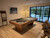Doc & Holliday Preakness Pool Table in Gray Walnut, modern pool table with pool cues and balls, in a stylish game room with wooden flooring and large glass doors leading to outdoor space.