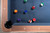 Doc & Holliday Preakness Pool Table in Gray Walnut, overhead view showing blue felt surface with pool balls scattered.
