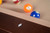 Doc & Holliday Zoey Pool Table, made in the USA, featuring a close-up view of the wooden edge with billiard balls in the background.
