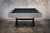 Doc & Holliday The Metalsmith Pool Table by Doc & Holliday, modern pool table with a sleek black felt surface and a silver and black finish, set against a concrete wall background.