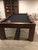 Doc & Holliday Paula Parsons Pool Table in Natural Walnut, a stylish wooden pool table with a black playing surface and rounded corner pockets.