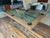 Doc & Holliday Kaci Slate Pool Table in Grey Walnut, showing a pool table with a green felt surface, wooden frame, and pool cues placed on top, in a room under setup or renovation.