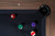 Doc & Holliday Kaci Slate Pool Table in Grey Walnut, showing a close-up of the black pool table corner with pool balls on the black felt surface, surrounded by a wooden frame.