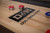 Doc & Holliday George Shuffleboard Table - Glazed Pearl Finish, close-up of the natural wood surface with shuffleboard pucks and the black logo of the brand.