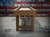 Wide profile view of Hank Shuffleboard Table in Oaklee finish showing table width, recessed scoring, and USA flag backdrop.