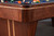 Doc & Holliday Preakness Slate Pool Table in Walnut & Maple, close-up of the sleek wooden corner and side panel with pool balls in the background.