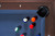 Doc & Holliday George Pool Table & Shuffleboard Combo - Antique Coffee, viewed from above showing billiard balls on the blue felt surface and a corner with wooden finish and a black cup holder.