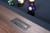 Doc & Holliday George Pool Table & Shuffleboard Combo in Gray Walnut, close-up of the wood surface with a metal plaque, and colorful billiard balls in the background.