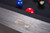 American Heritage Billiards Alta Pool Table in Marble Grey, close-up of the textured wood grain surface with a metal plaque and pool balls in the background.