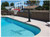 First Team Inc First Team HYDROSHOT | Adjustable Pool Side Basketball Hoop, mounted beside a swimming pool on a concrete deck with clear blue water and a backyard fence in the background.