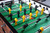 A mid-game moment with rods in motion and the foosball mid-play. Slight blur adds energy while the focus remains on the table’s refined lines and impeccable construction.

