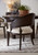 Hooker Furniture Retreat Cane Barrel Back Dark Wood Chair, shown on a dining room rug with a dark wood table and decorative plant in background.