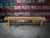 Side profile of the Doc & Holliday Hank shuffleboard table in distressed Rustic Silver Brown Oak, featuring clean lines and American flag backdrop