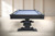 Environmental end view of the Beaumont Black Ash pool table, showing the Academy Blue felt, steel name plate, solid ash wood grain, pedestal base, and true 3-piece slate billiard table design.