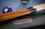 Close-up of the Plank & Hide Co. steel name plate on the Beaumont Black Ash pool table, styled with cue sticks, Championship Academy Blue felt, and the Doc & Holliday luxury billiard ball set.