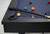 Plank & Hide Co Isaac Slate Pool Table in Black Ash, with billiard balls and cues on the table surface.