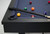 Plank & Hide Co Isaac Slate Pool Table in Black Ash, close-up view showing sleek black ash wood frame and blue felt surface with pool balls and cue sticks.