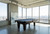 C.L. Bailey Adrian Slate Pool Table, modern pool table with a sleek black finish situated in a high-rise space with large windows overlooking a city skyline.