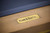 Plank & Hide Deco name plate close-up on the Glazed Maple slate pool table with golden brass accents, exclusive to Sawyer Twain.