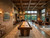 Doc & Holliday Derby Shuffleboard Table in Walnut,  a luxurious game room with modern furniture, large windows overlooking greenery, brick and stone walls, and vintage lighting.