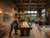 Doc & Holliday Derby Shuffleboard Table in Walnut, indoor recreation space with people playing shuffleboard and relaxing in a cozy, well-lit lounge.