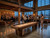 Doc & Holliday Derby Shuffleboard Table in Walnut, in an industrial-style loft bar setting with large windows and people enjoying drinks and playing shuffleboard.