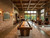 Doc & Holliday Derby Shuffleboard Table in Walnut, a sleek wooden shuffleboard table with a polished surface in a spacious, well-lit game room with brick and stone walls, leather chairs, and large windows with scenic views.