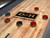 Doc & Holliday Derby Shuffleboard Table in Walnut, shot of the wooden shuffleboard surface with puck markings, pucks, and a central logo.