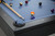 Doc & Holliday Peter Parsons Slate Pool Table in Matte Black Lacquer, close-up of the pool table with billiard balls and cues arranged on the blue felt surface.