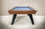 Doc & Holliday The Bellano Slate Pool Table in Matte Brandwine, front view of the pool table with blue felt surface, wooden frame, and black legs, set against a textured beige wall.