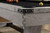 Playcraft Yukon Slate Pool Table 8' – Northern Drift or Fieldstone Finish with White Glove Install, close-up of the corner showing the light-colored textured wood finish, black metal corner accents, and part of the black felt playing surface with pool balls and cue ball.