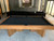 Doc & Holliday Infinity Slate Pool Table with black felt, wooden frame, and sturdy legs in a modern living room setting, perfect for game room entertainment.