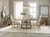 Hooker Furniture Affinity 48-inch Round Pedestal Dining Table with 1-18 inch Leaf, shown in a modern dining room setting with beige chairs, a floral centerpiece, and natural lighting.