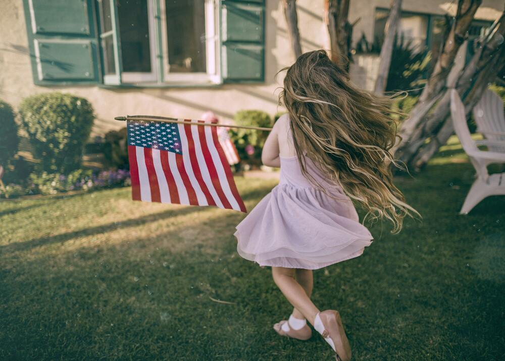 a little girl running outdoors holding an American flag with patio chairs in the background